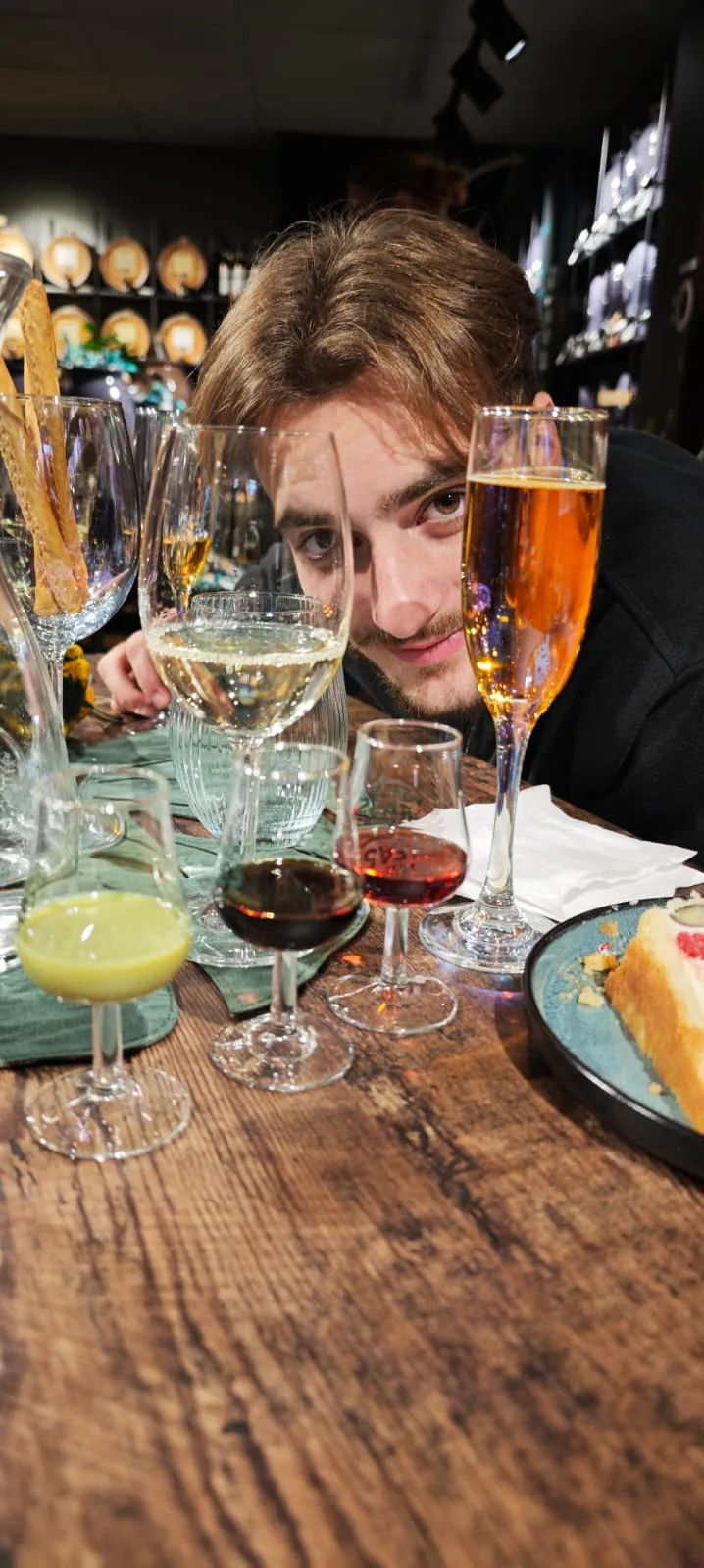 Junger Mann blickt neugierig über eine Reihe gefüllter Verkostungsgläser mit Wein und Aperitifs